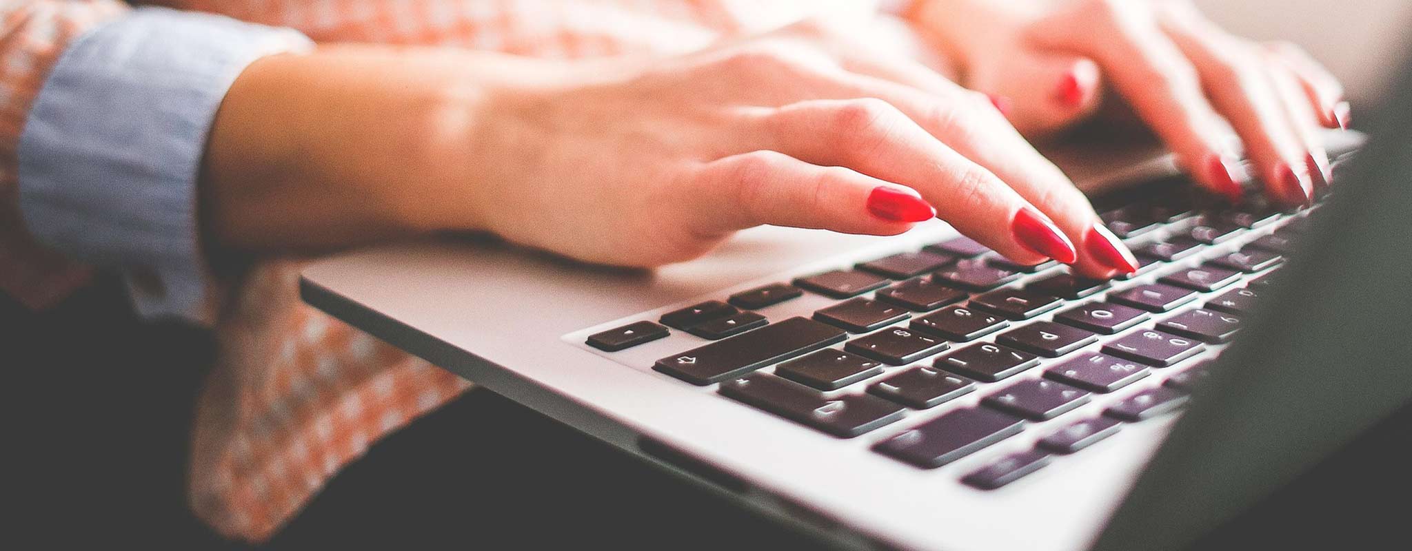 Kvinna har har en laptop i knät. Hon skriver på tangentbordet.