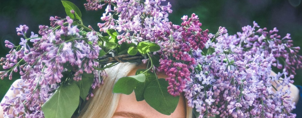 En kvinna bär en midsommarkrans. Kransen är gjord av syrenblommor.