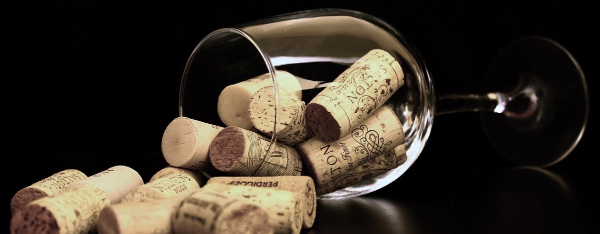 Ett vinglas ligger på ett bord. I glaset, och även utanför, ligger vinkorkar.