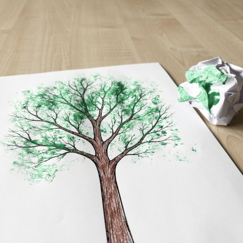 Färglagd målarbild av ett träd där gröna löv har skapats genom att dutta färg med en hopknycklad pappersbit; pappersbiten med grön färg ligger bredvid.